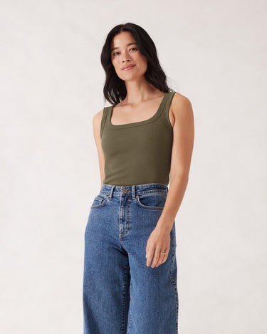 Woman wearing a green tank top and blue jeans against a white background